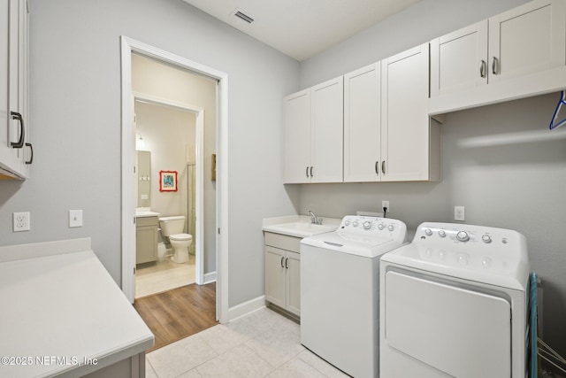 clothes washing area featuring light tile patterned floors, washing machine and clothes dryer, visible vents, cabinet space, and a sink