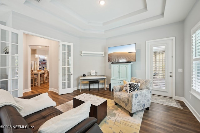 living area with a raised ceiling, wood finished floors, baseboards, and a wall mounted AC