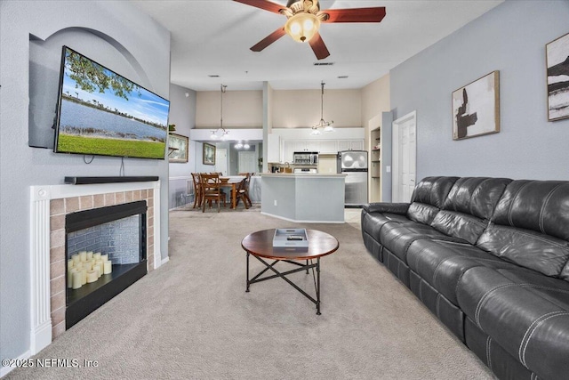 living room featuring a fireplace, ceiling fan, visible vents, and light colored carpet