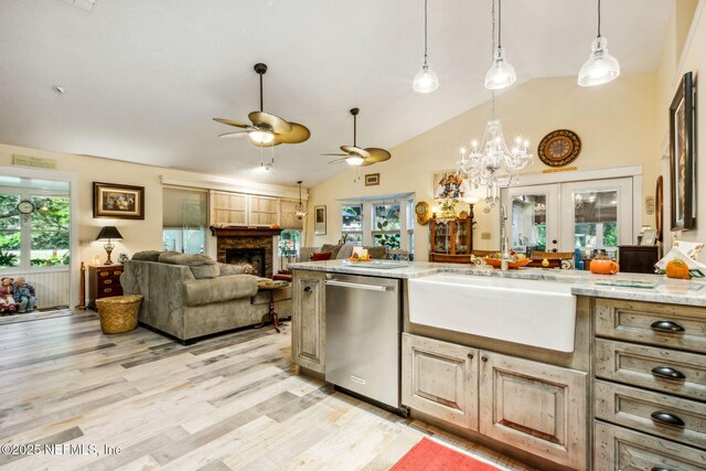 kitchen featuring light wood finished floors, a stone fireplace, a sink, ceiling fan with notable chandelier, and stainless steel dishwasher