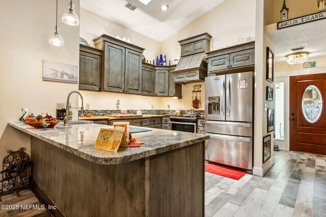 kitchen with a sink, premium range hood, a peninsula, stainless steel appliances, and visible vents