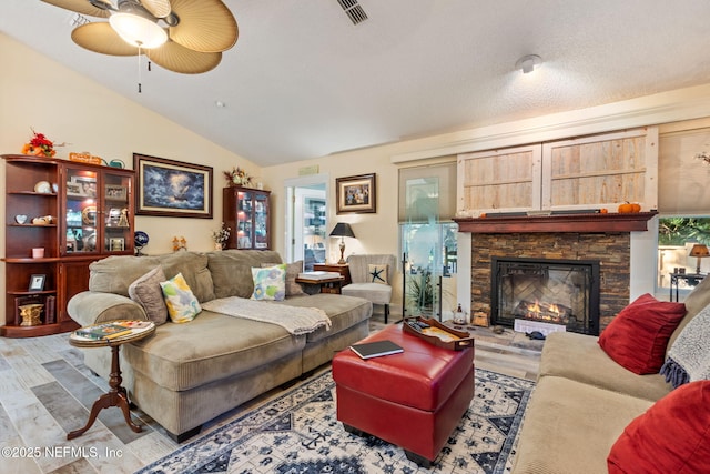 living room featuring vaulted ceiling, ceiling fan, visible vents, a stone fireplace, and wood finished floors