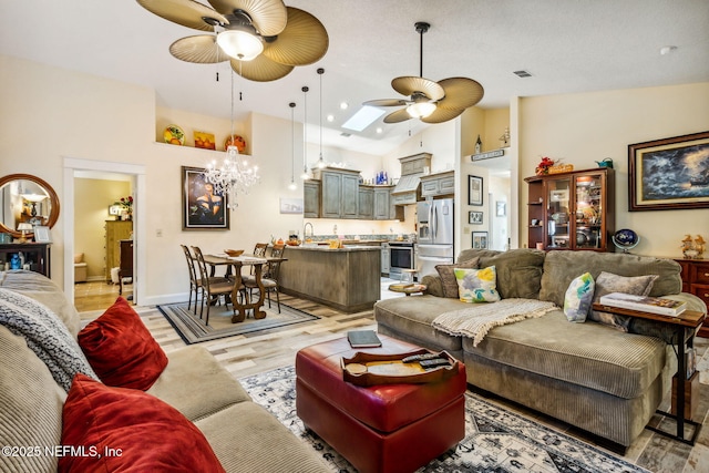 living area featuring high vaulted ceiling, light wood finished floors, baseboards, recessed lighting, and ceiling fan with notable chandelier