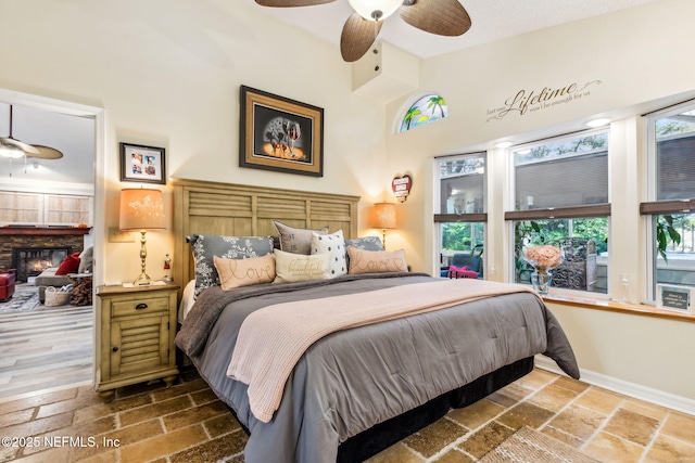 bedroom featuring a high ceiling, a glass covered fireplace, baseboards, and ceiling fan