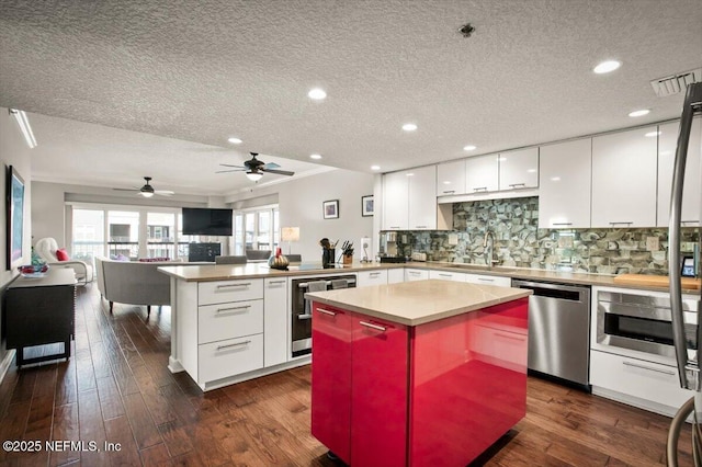 kitchen with a peninsula, appliances with stainless steel finishes, dark wood-type flooring, white cabinetry, and a sink