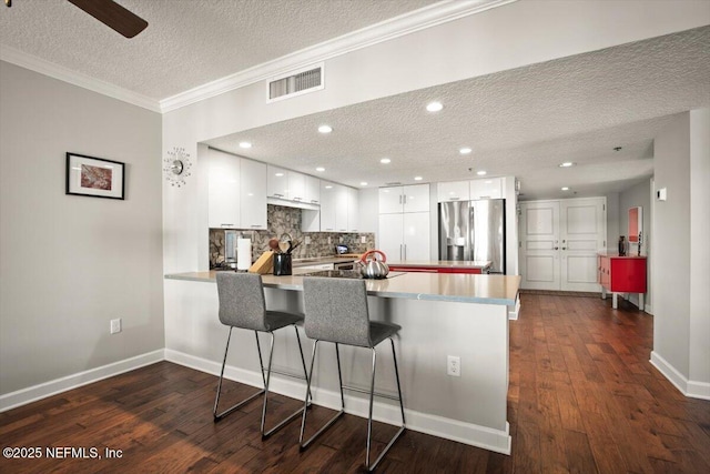 kitchen with white cabinetry, stainless steel fridge with ice dispenser, dark wood finished floors, visible vents, and a peninsula