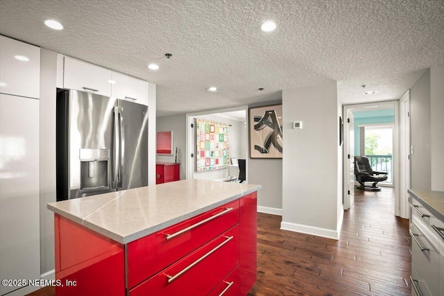 kitchen featuring a kitchen island, a textured ceiling, dark wood-style floors, stainless steel refrigerator with ice dispenser, and baseboards