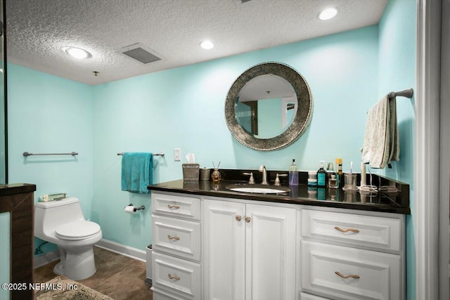 bathroom with a textured ceiling, visible vents, baseboards, toilet, and vanity