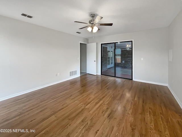 empty room with wood finished floors, baseboards, ceiling fan, and visible vents