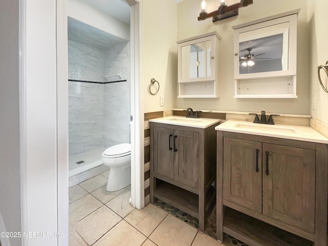 full bathroom with tile patterned floors, a tile shower, toilet, vanity, and ceiling fan
