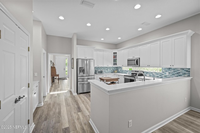 kitchen with visible vents, white cabinets, a peninsula, stainless steel appliances, and light wood-style flooring