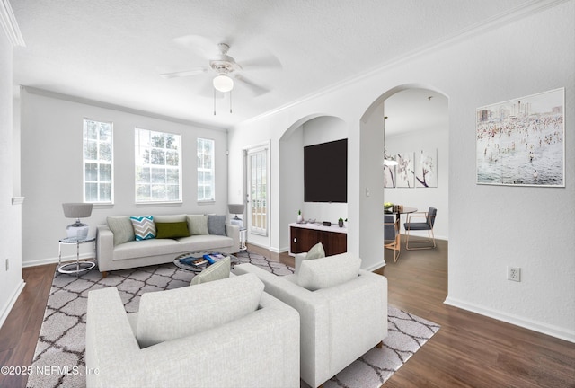 living room with a ceiling fan, ornamental molding, baseboards, and wood finished floors