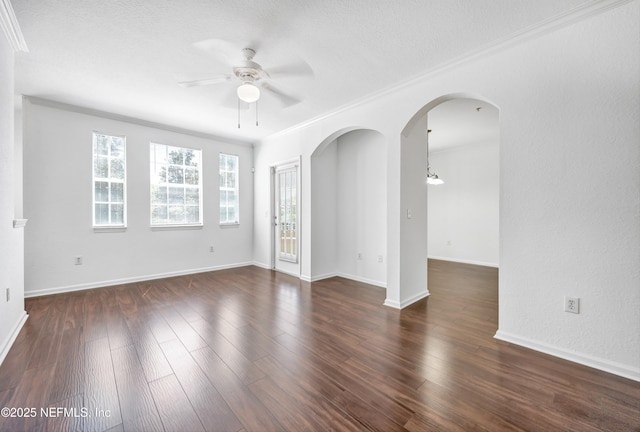 unfurnished room featuring arched walkways, crown molding, a ceiling fan, and dark wood finished floors