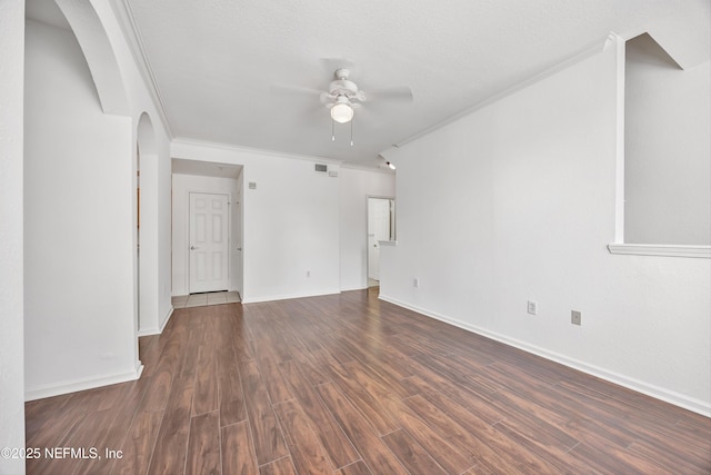 empty room featuring ornamental molding, baseboards, arched walkways, dark wood-style floors, and a ceiling fan