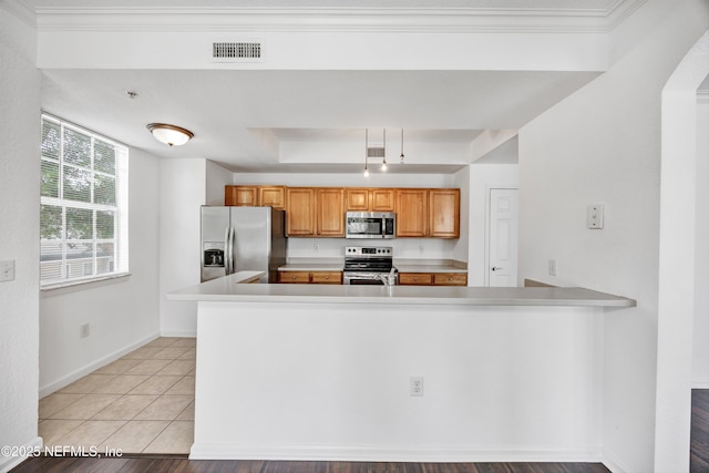 kitchen featuring light countertops, a peninsula, brown cabinetry, light tile patterned floors, and stainless steel appliances