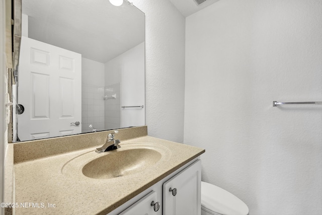 bathroom with a shower, toilet, vanity, and a textured wall
