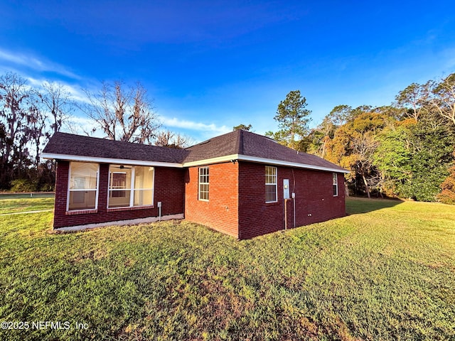 view of property exterior with a ceiling fan, brick siding, and a yard