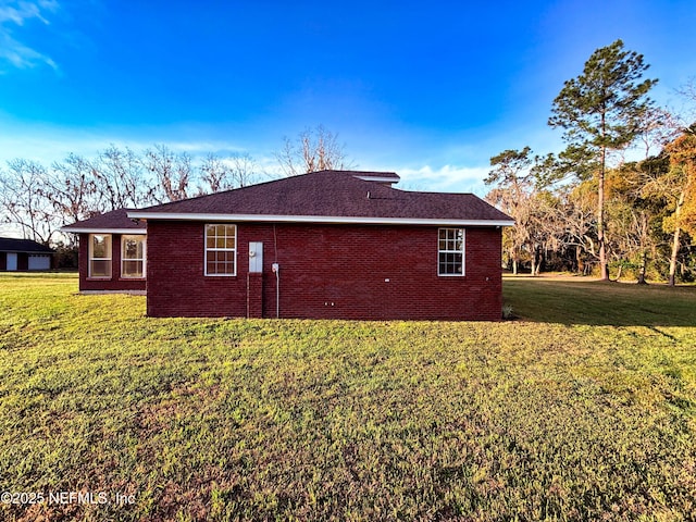 view of property exterior with roof with shingles, brick siding, and a yard