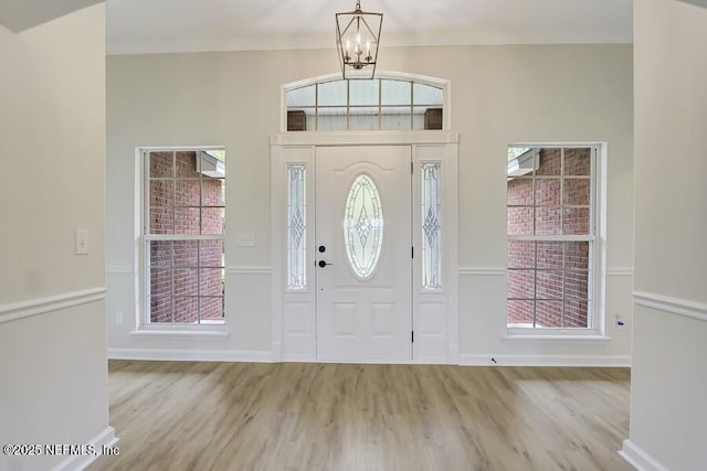 entryway with a chandelier, baseboards, ornamental molding, wood finished floors, and a wealth of natural light