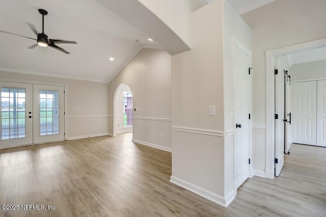 empty room with light wood finished floors, lofted ceiling, baseboards, arched walkways, and ceiling fan