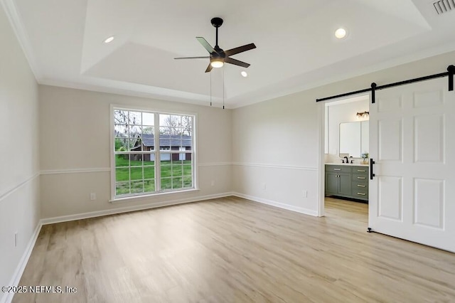 spare room featuring a tray ceiling, a barn door, light wood-type flooring, visible vents, and ceiling fan