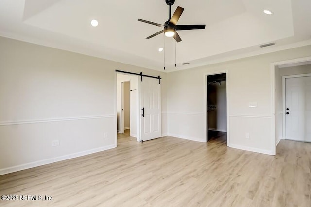 interior space with a ceiling fan, a tray ceiling, light wood finished floors, and visible vents