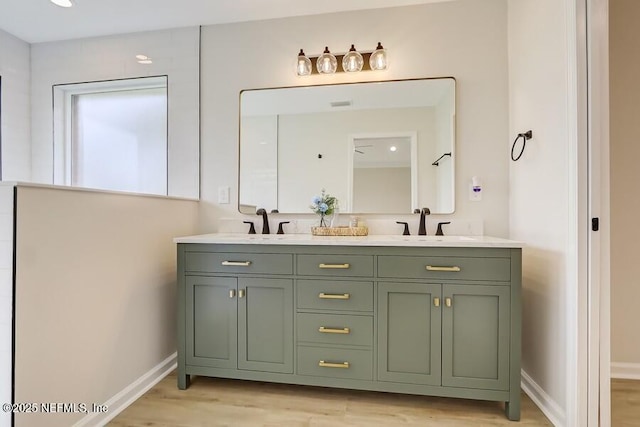 full bath with baseboards, wood finished floors, double vanity, and a sink