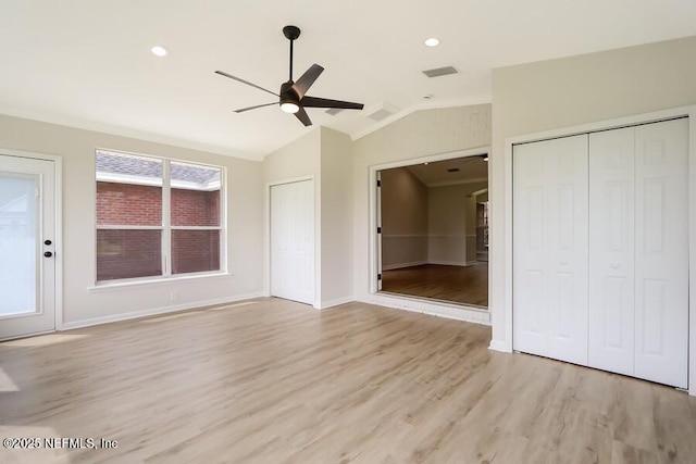 unfurnished bedroom with multiple closets, lofted ceiling, baseboards, visible vents, and light wood-style floors