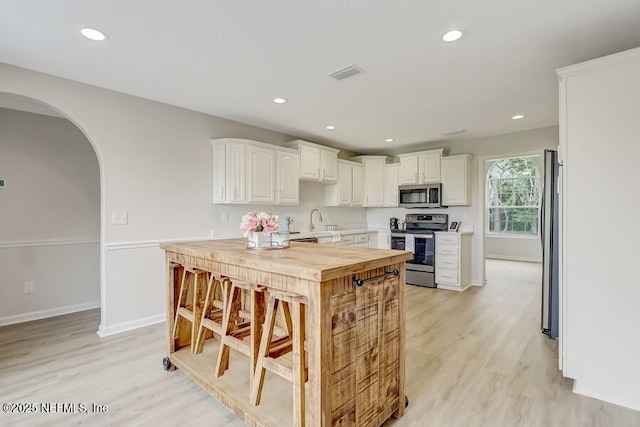 kitchen with arched walkways, appliances with stainless steel finishes, light wood finished floors, and visible vents