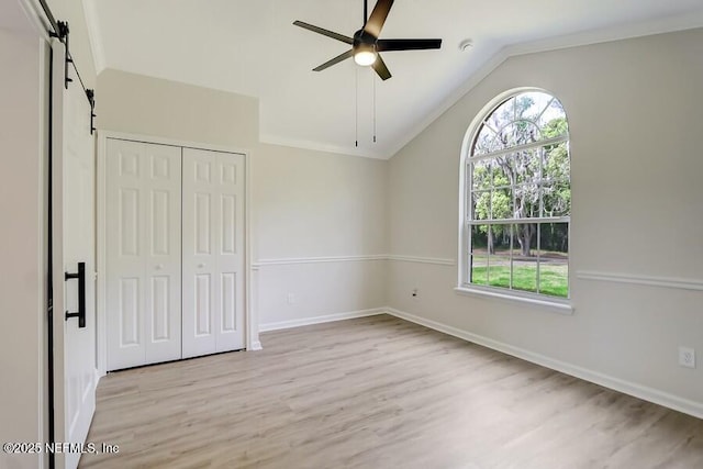 unfurnished bedroom featuring a closet, light wood finished floors, baseboards, a barn door, and lofted ceiling