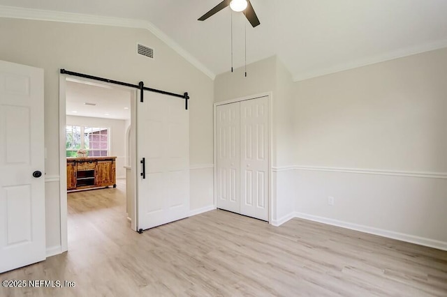 unfurnished bedroom featuring visible vents, light wood finished floors, baseboards, a barn door, and vaulted ceiling