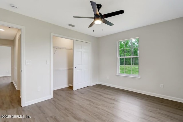 unfurnished bedroom featuring a closet, a ceiling fan, wood finished floors, baseboards, and visible vents