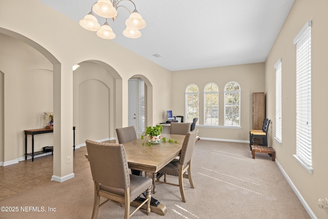 dining room featuring baseboards, arched walkways, carpet floors, and a chandelier