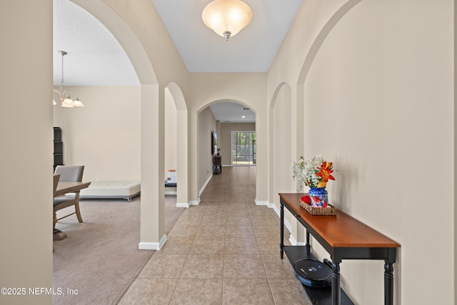 hallway featuring carpet, baseboards, tile patterned floors, arched walkways, and a notable chandelier
