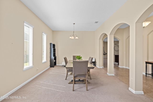 dining room with carpet flooring, visible vents, baseboards, arched walkways, and an inviting chandelier