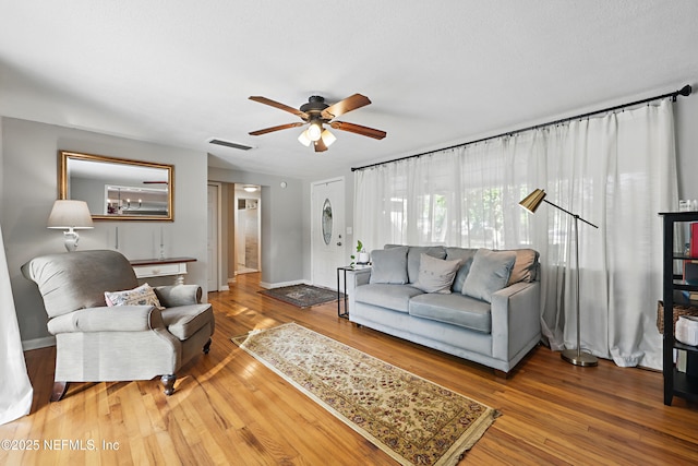 living area featuring baseboards, visible vents, wood finished floors, and ceiling fan
