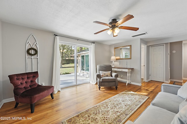 living area with wood finished floors, a textured ceiling, baseboards, visible vents, and ceiling fan