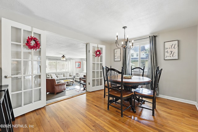 dining space with french doors, wood finished floors, a textured ceiling, baseboards, and an inviting chandelier