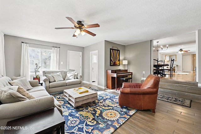 living room featuring ceiling fan with notable chandelier, baseboards, a textured ceiling, and wood finished floors