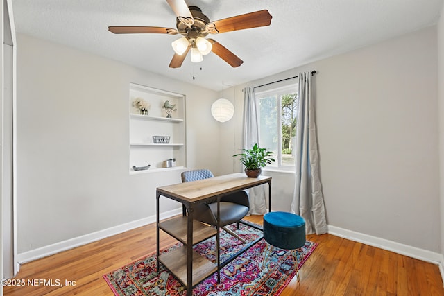 home office featuring baseboards, a ceiling fan, wood finished floors, and built in shelves