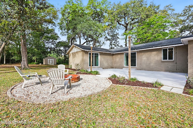 rear view of property with a fire pit, a patio area, a shed, stucco siding, and an outbuilding