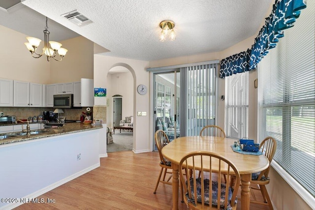 388 Lolly Ln, Saint Johns, FL 32259 - dining area with a textured ceiling, visible vents, arched walkways, an inviting chandelier, and light wood-style flooring