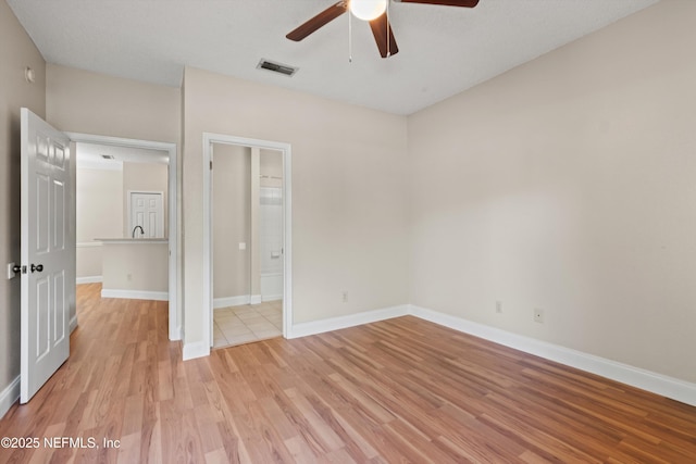 unfurnished bedroom featuring light wood-style flooring, visible vents, baseboards, a ceiling fan, and ensuite bath