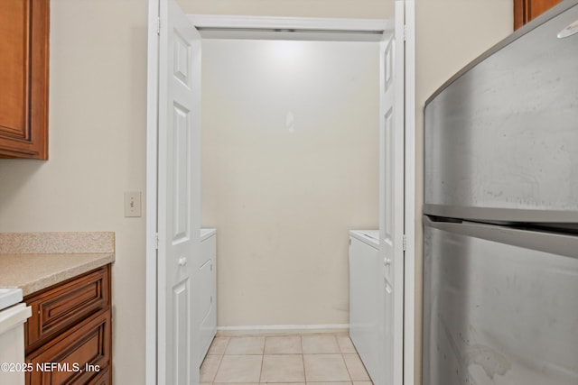 interior space featuring light countertops, light tile patterned flooring, freestanding refrigerator, washing machine and dryer, and brown cabinetry