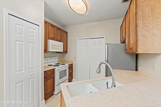 kitchen featuring light countertops, white appliances, a sink, light tile patterned flooring, and brown cabinets