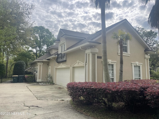 view of side of property with concrete driveway, stucco siding, and roof with shingles