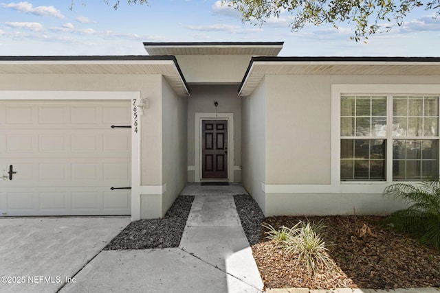 view of exterior entry with stucco siding, driveway, and a garage
