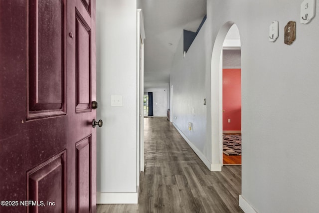 hallway with arched walkways, baseboards, and dark wood-type flooring