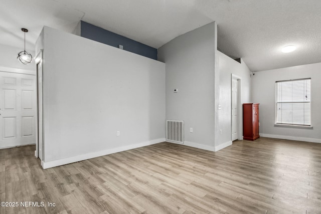 unfurnished room featuring lofted ceiling, baseboards, a textured ceiling, visible vents, and wood finished floors
