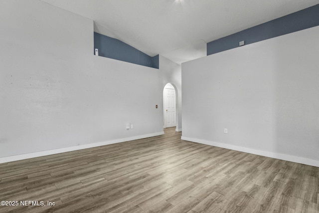 unfurnished room with baseboards, high vaulted ceiling, wood finished floors, and arched walkways